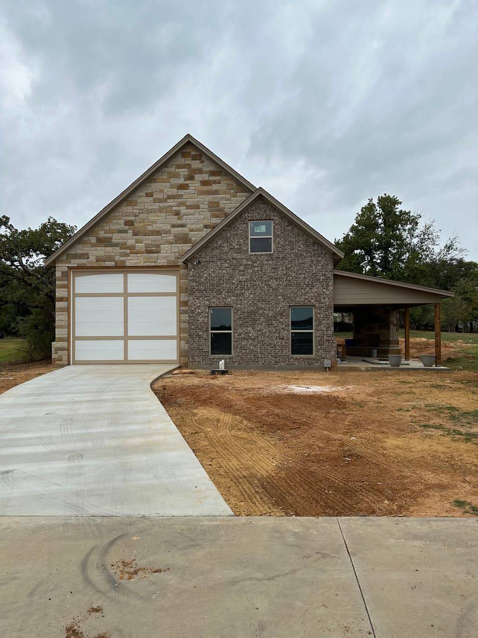 Stone and brick building with a tall white garage door and a covered patio beside it