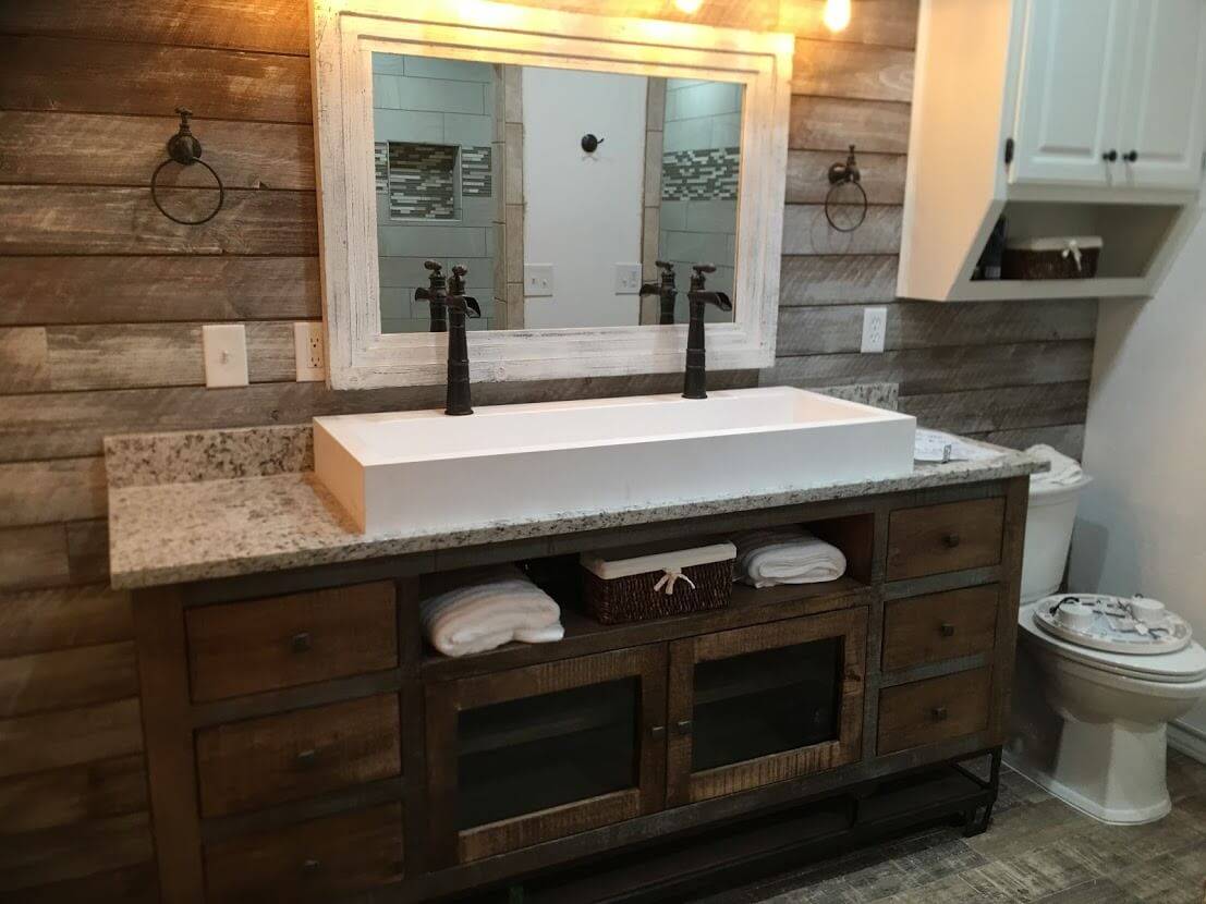Bathroom with a wide white trough sink, dark faucets, a wood plank wall and a rustic double vanity