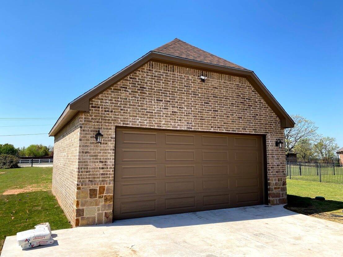Brick garage with a tan two-car door, stone corners and lantern lights