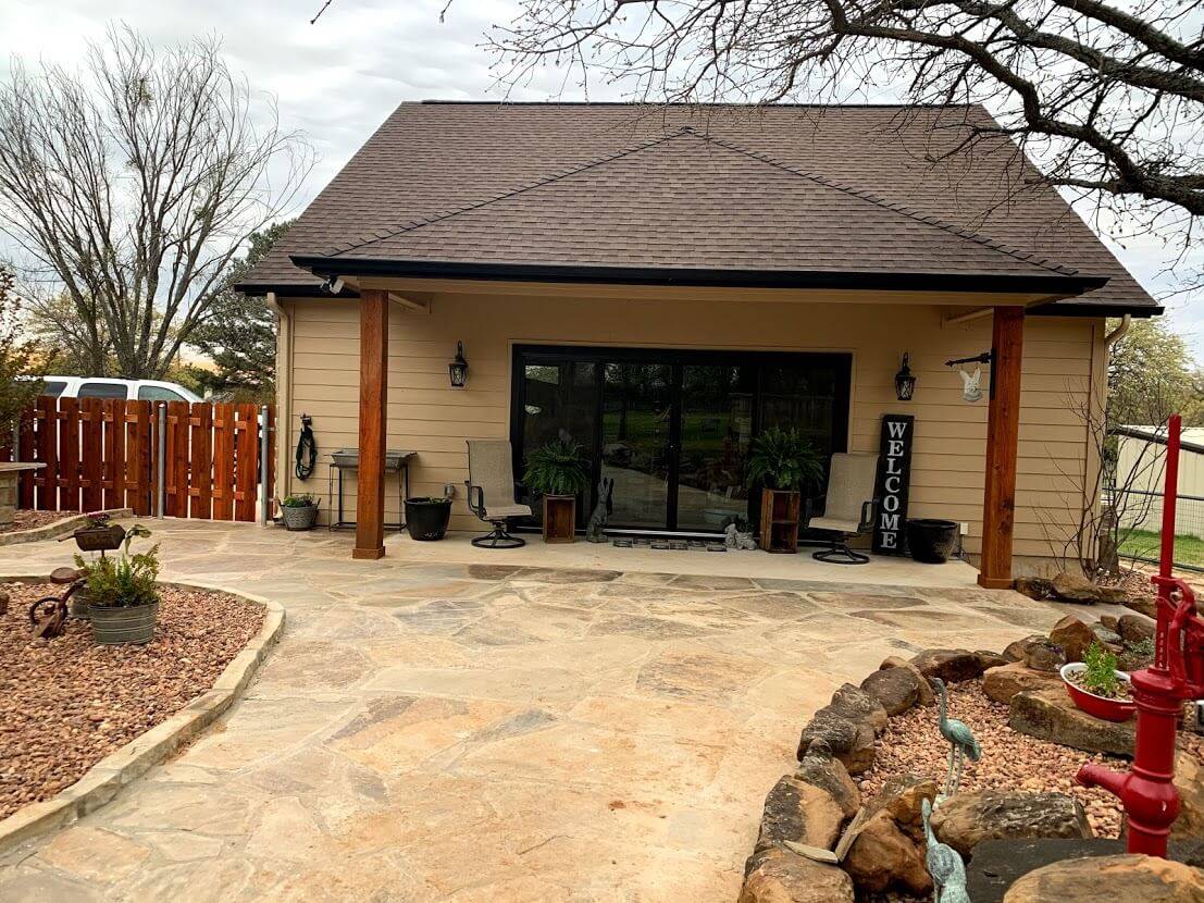 Covered porch with cedar posts and sliding glass doors, in front of a flagstone patio