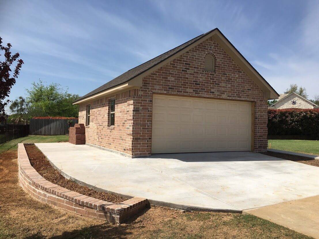 Brick garage with a cream garage door, a new concrete drive and a curved brick planter wall